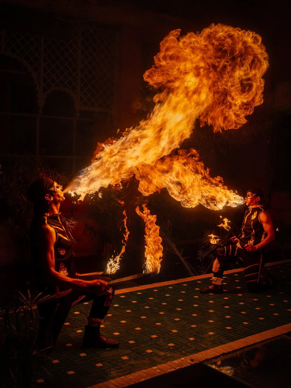 Deux cracheurs de feu projetant de grandes flammes dans un patio du Palais Jad Mahal